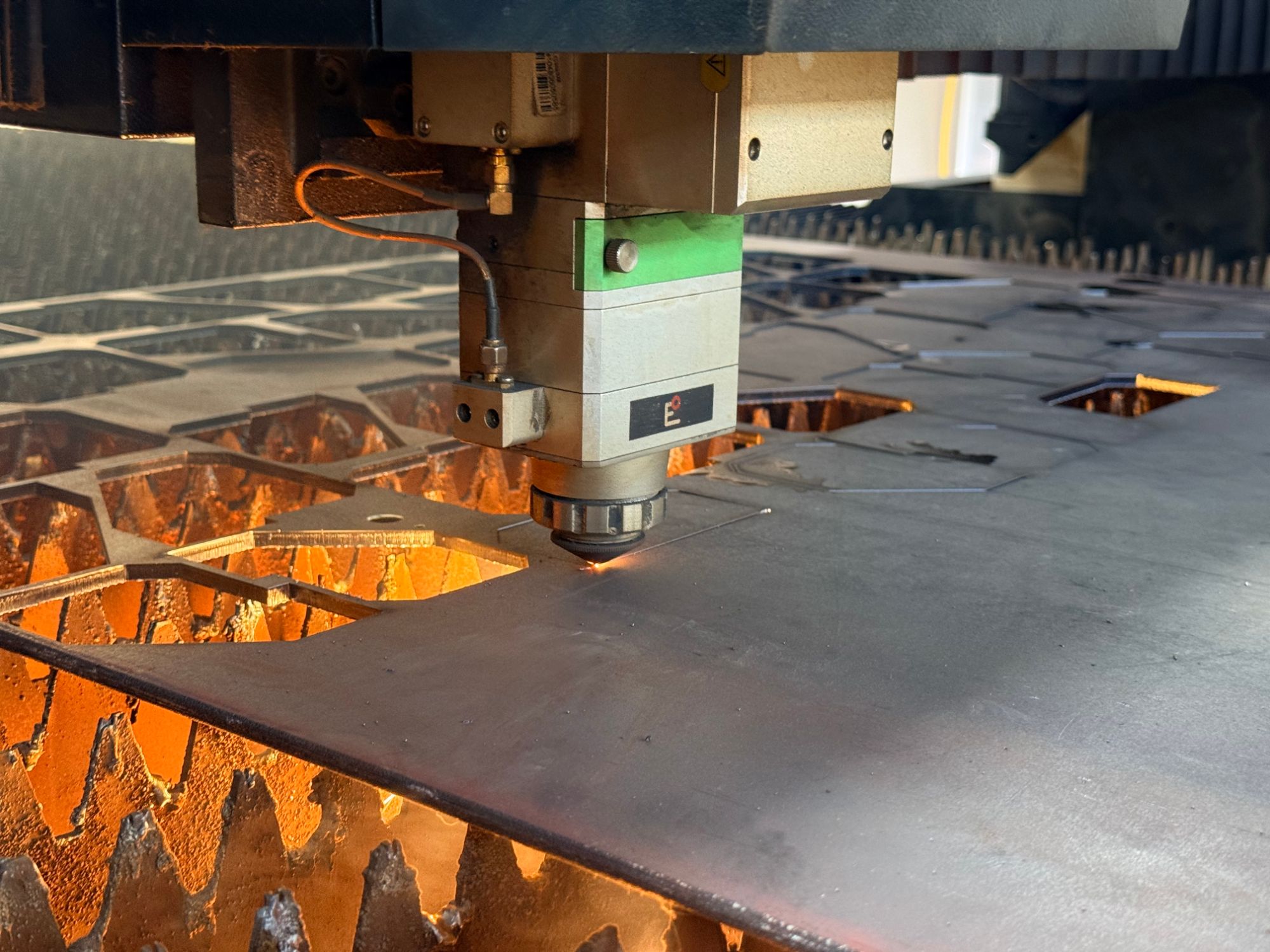 Close-up of a fiber laser cutting head with sparks while cutting metal